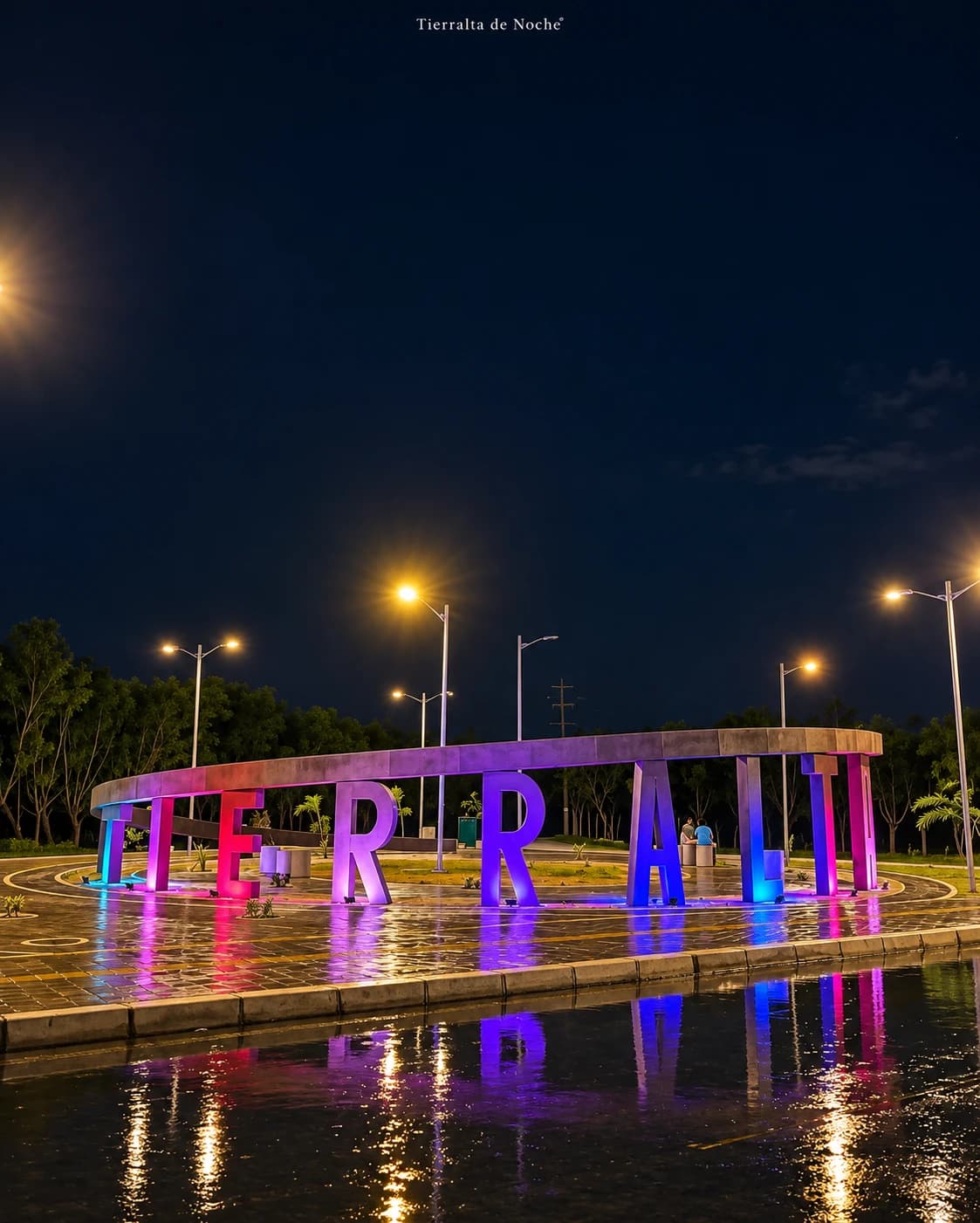 Letrero luminoso de Tierralta de noche, con las letras iluminadas en rosa y azul y su reflejo en el agua.
